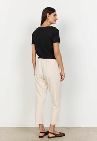 Black cotton T-shirt with short sleeves, paired with cream tapered trousers. Brown woven sandals and simple gold earrings complete the outfit.