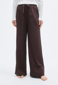 Pantalon large marron avec taille élastique et cordon de serrage. Confectionné dans un tissu lisse, il présente une coupe décontractée et une longueur pleine.