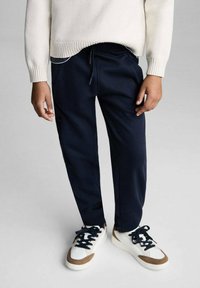 Marinblå joggingbyxor med elastisk midja och dragsko, matchade med vita och bruna sneakers med svarta snören. Texturerad, avslappnad design.