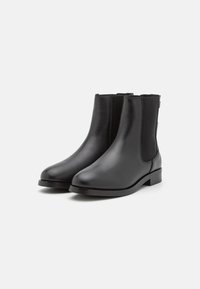 Bottines en cuir noir avec une texture lisse, bout rond et panneaux latéraux élastiques. Talon bas et épais avec des détails de couture subtils.