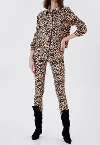 Chaqueta de mezclilla con estampado de leopardo y leggings en tonos beige y marrón, combinados con botas negras hasta la rodilla. Tejido texturizado con detalles de botones.