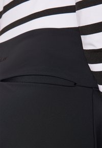Pantalón de tela negra con un bolsillo oculto. La parte superior presenta rayas horizontales blancas y negras. Textura suave con un diseño ajustado.