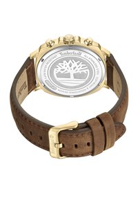 Timberland pulksteņi ar brūnu ādas siksnu un zelta tonī nerūsējošā tērauda korpusu. Aizmugurē atrodas logo un ūdensnoturības detaļas.