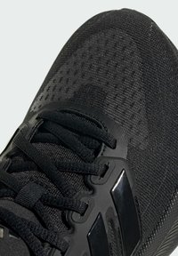 Chaussure de sport noire avec une tige en maille texturée, fermeture à lacets et accents noirs brillants. Comprend un amorti à air et un bout renforcé.