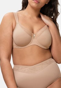 Sujetador beige claro con copas moldeadas, tirantes ajustables y cierre de gancho. Textura suave y un ligero brillo; diseñado para comodidad y soporte.