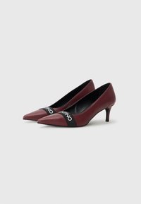 Tacchi alti in pelle borgogna con punta affusolata, caratterizzati da una fascia nera con logo a livello del collo del piede e un tacco moderato.