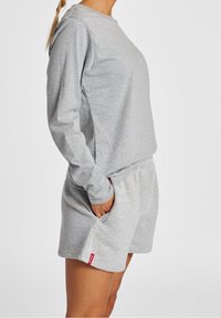Harmaa huppari pitkilla hihoilla ja pyöreällä kaula-aukolla, yhdistettynä matching harmaisiin shortsseihin, joissa on taskut ja punainen logotehoste. Pehmeä kangas.