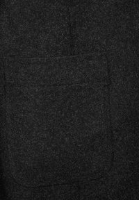 Tissu texturé gris foncé avec une grande poche carrée appliquée sur la surface, montrant des lignes de couture subtiles.