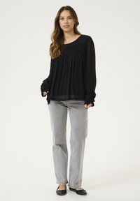 Blusa nera trasparente con tessuto testurizzato, arricciata sulle spalle, abbinata a jeans grigio chiaro a gamba dritta e ballerine nere.