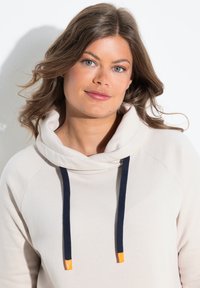 Lichtbeige hoodie met een kraag, marineblauwe trekkoorden met oranje uiteinden en een zachte textuur. Ontworpen met een relaxte pasvorm en raglanmouwen.