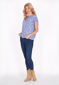 Top blu con motivo paisley, maniche corte, abbinato a jeans skinny scuri e stivali col tacco color beige. Tessuto morbido e vestibilità casual.