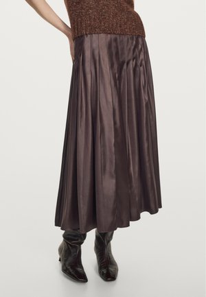 Gonna lunga plissettata in satin marrone scuro. Presenta una texture morbida e si posa in vita, completata da stivali neri aderenti alla caviglia.