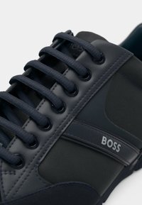 Navy blue sneaker made of leather and fabric with round laces, reinforced eyelets, and a side logo. Features a textured panel and smooth accents.