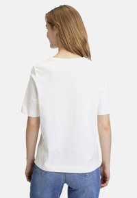 T-shirt en coton blanc à manches courtes, avec un col rond et des détails de couture contrastants. Le dos présente un design simple et lisse.