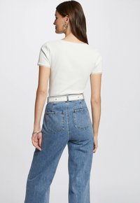Haut blanc à manches courtes avec un ourlet en dentelle, associé à un jean en denim bleu clair taille haute avec deux poches à l'arrière et une coupe large.