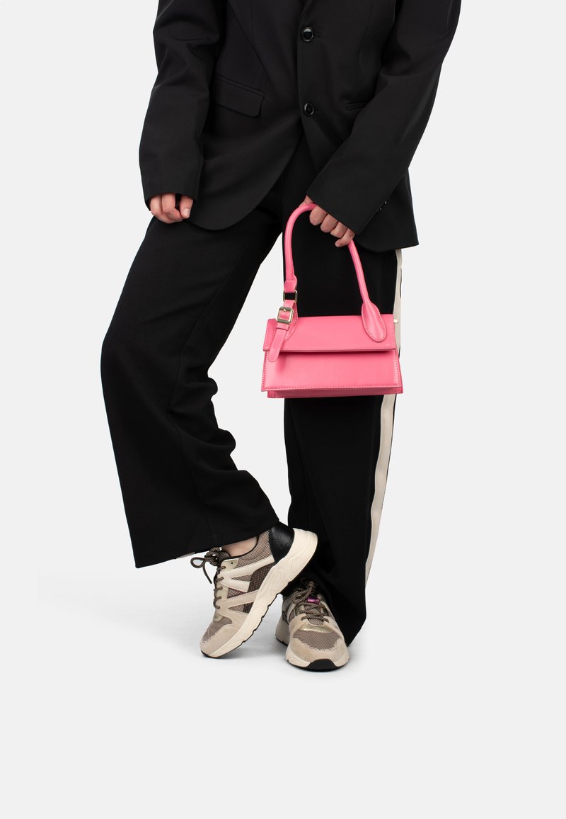 Bolso de mano de cuero rosa con un diseño estructurado y un asa superior, que presenta un cierre, combinado con pantalones de pierna ancha negros y zapatillas con estampado.