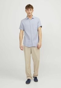 Lichtblauwe kortemouw knoopshirt met een borstzak, gecombineerd met beige losse broek en marineblauwe sneakers. Gladde textuur, casual ontwerp.