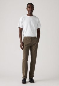White short-sleeve t-shirt paired with khaki-colored slim-fit pants. Textured fabric, clean lines, and a buttoned front pocket are visible.