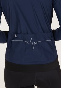 Maglietta a maniche lunghe blu navy con grafica a linea del battito cardiaco in bianco sul retro. Presenta una tasca con zip e una vita nera aderente.
