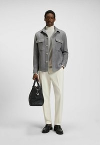 Gray button-up wool jacket with two chest pockets, white turtleneck, cream trousers, black bag, and leather loafers. Smooth texture overall.