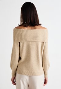 Off-the-shoulder beige sweater made of soft knit fabric, featuring ribbed accents at the neckline and hem, with balloon sleeves.