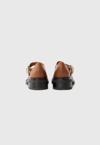 Chaussures en cuir marron avec un bout rond, semelle en plateforme noire et un détail de boucle décoratif sur le côté. Texture lisse, design simple.