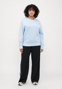 Helles blaues Sweatshirt mit Rundhalsausschnitt und langen Ärmeln, mit gesticktem "Tommy Hilfiger"-Logo, kombiniert mit schwarzen weit geschnittenen Hosen.