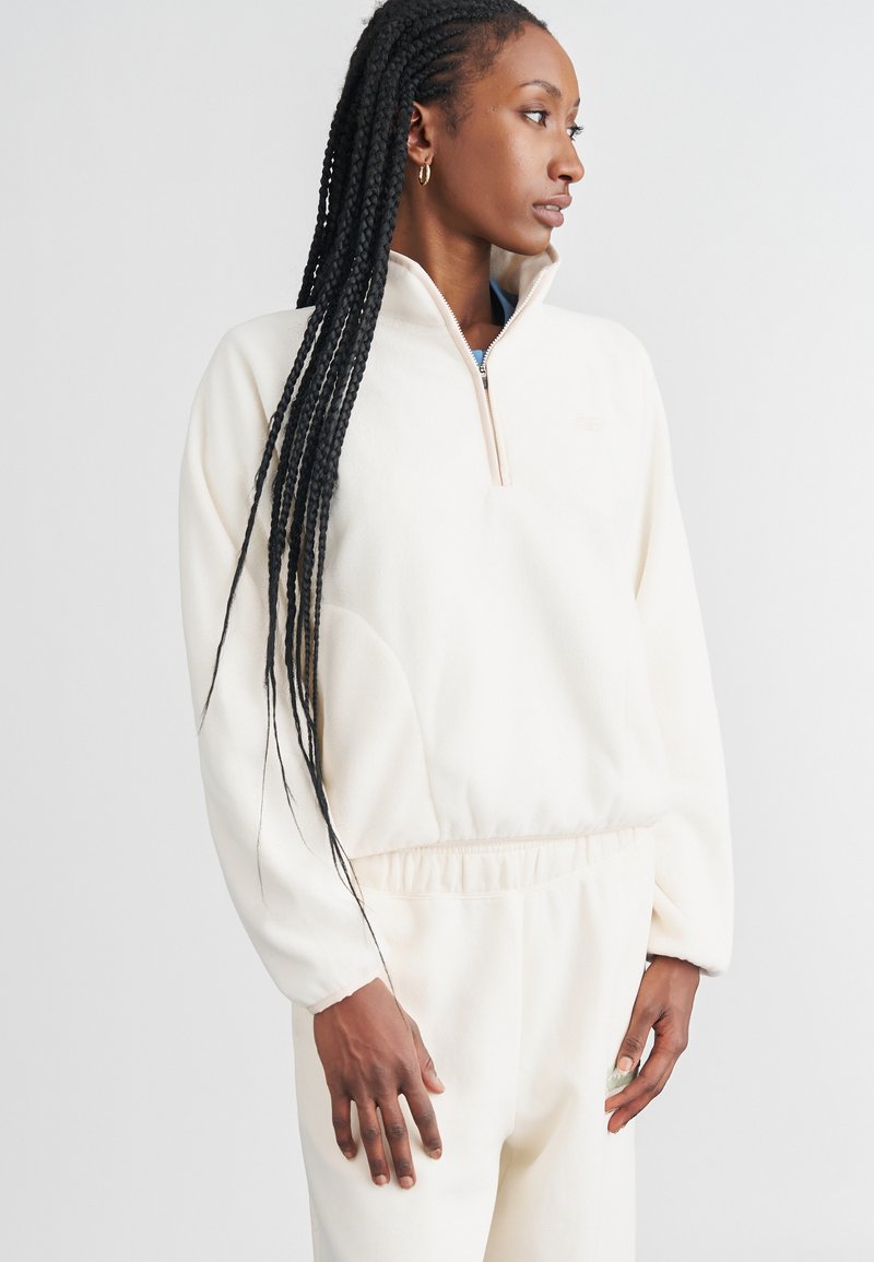 Pullover in pile color crema con collo a mezza zip, maniche lunghe e vita elastica. Presenta una texture liscia e un design minimalista.
