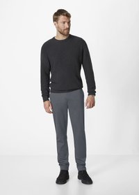 Dark gray knitted sweater paired with light gray pants. Model displays a relaxed fit. Black footwear completes the look.