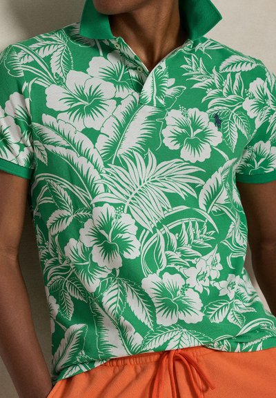 Πράσινο πόλο με λευκό τροπικό λουλουδάτο σχέδιο, με αντιθετικό πράσινο γιακά. Το υλικό φαίνεται υφή και διαπνέον.