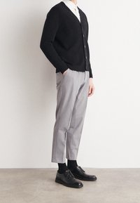 Svart stickad cardigan, grå skräddarsydd byxor, svarta skor och strumpor. Cardiganen har v-ringning och knappar. Slim fit, korta byxor.