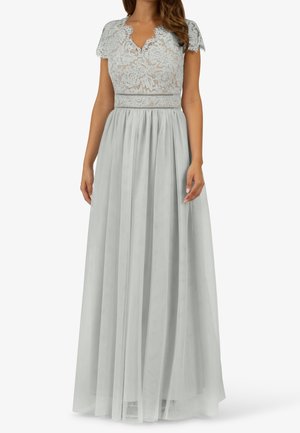 Kobieta ubrana w suknię do podłogi w jasnoszarym kolorze, z koronkowymi krótkimi rękawami, kwiatowym koronkowym gorsetem i plisowaną spódnicą z szyfonu.