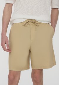 Pantaloni corti beige in un tessuto leggero con vita elasticizzata e cordoncino, dotati di tasche laterali, progettati per un fit comodo.