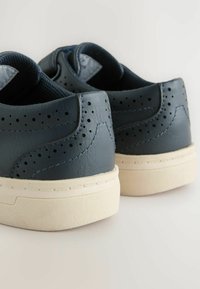 Ciemnoniebieskie skórzane sneakersy z perforowanymi detalami po bokach, kremowymi gumowymi podeszwami i teksturowanym wykończeniem na pięcie.