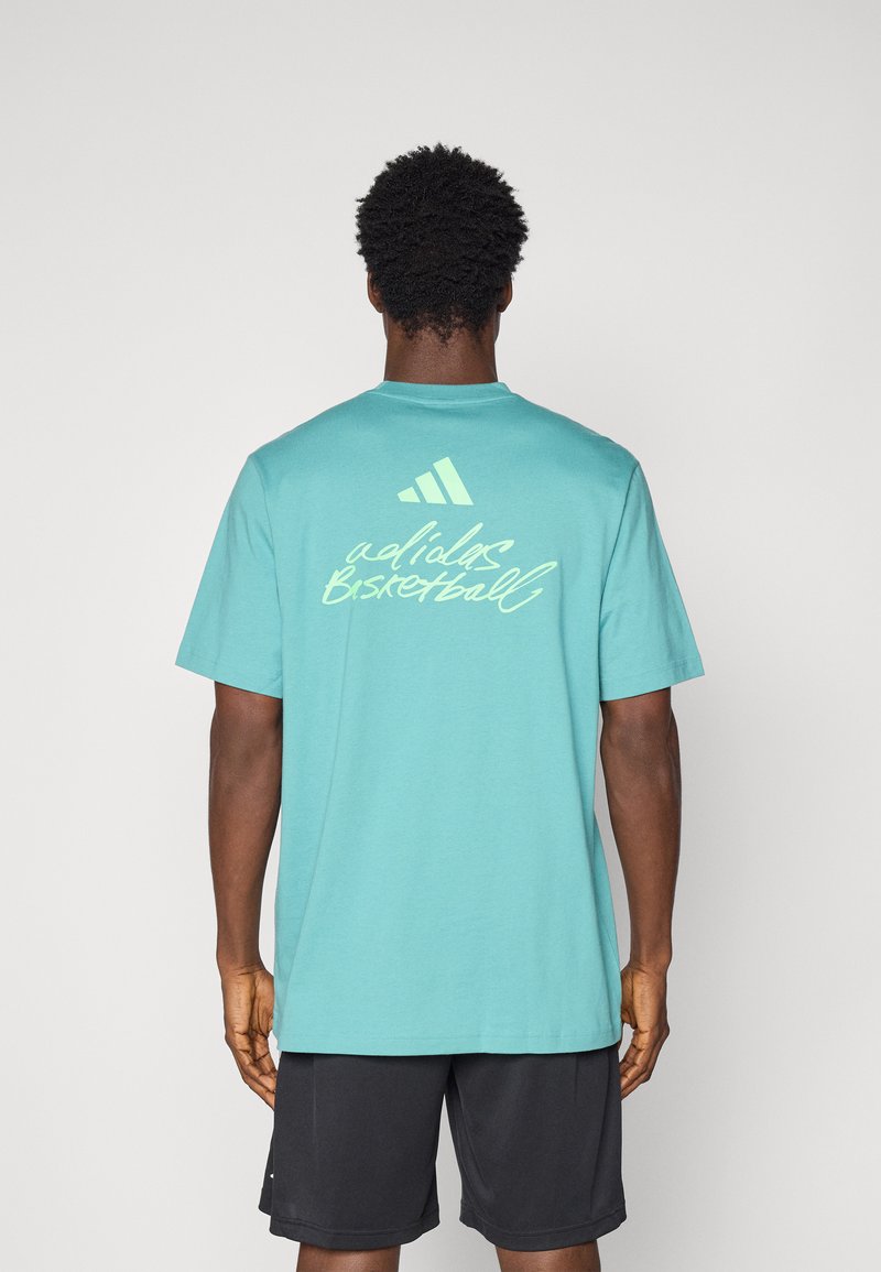Camiseta de algodón turquesa con mangas cortas, que presenta el texto blanco "adidas Basketball" y el logo en la parte posterior. Textura suave, diseño de cuello redondo.