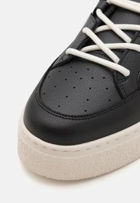 Must musta sneaker perforatsiooniga varvastega, valged paelad ja tekstureeritud platvormi tald heledas beežis toonis.