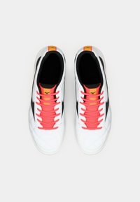 White athletic shoes with black accents, featuring diamond pattern texture and bright pink laces. Yellow logo on the tongue.