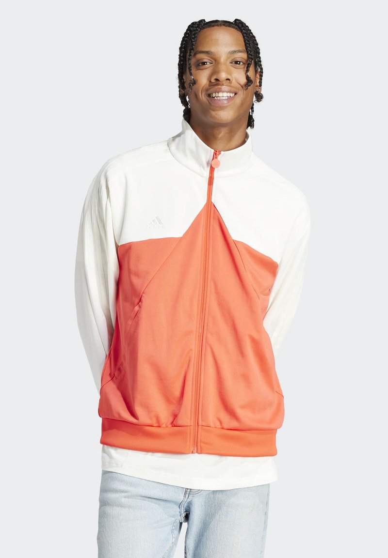 Veste de sport orange et blanche avec un col montant, fermeture éclair et poches avant. Tissu doux avec des sections de couleurs contrastées.