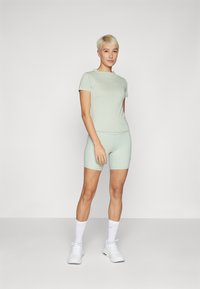 Lysegrønn tettsittende T-skjorte og matchende sykkelshorts laget av glatt, elastisk stoff. Kombinert med hvite joggesko og sokker.