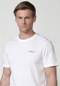 T-shirt bianca a maniche corte con un design a righe testurizzate, scollatura rotonda e piccolo logo nero sul lato sinistro del petto.