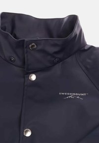 Donker marineblauwe waterdichte jas met hoge kraag. Voorzien van zilveren hardware en logo. Glad textuur met een strakke, moderne uitstraling.