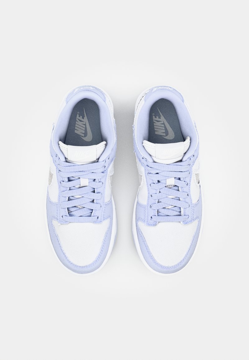 Zapatillas Nike blancas y azul claro con tejido texturizado, cordones planos, cuello acolchado y suelas de goma. Presenta un logo bordado en los laterales.