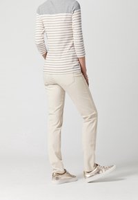 Maglietta a maniche lunghe a righe grigia e beige con maniche a tre quarti, abbinata a pantaloni color crema e sneakers metalliche.