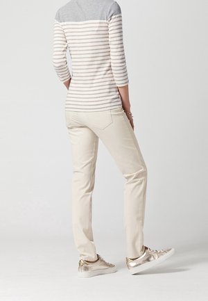 Maglietta a maniche lunghe a righe grigia e beige con maniche a tre quarti, abbinata a pantaloni color crema e sneakers metalliche.