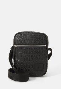 Černá obdélníková crossbody taška vyrobená z texturovaného materiálu, s embosovanou značkou, stříbrným zipem a tkaným popruhem.