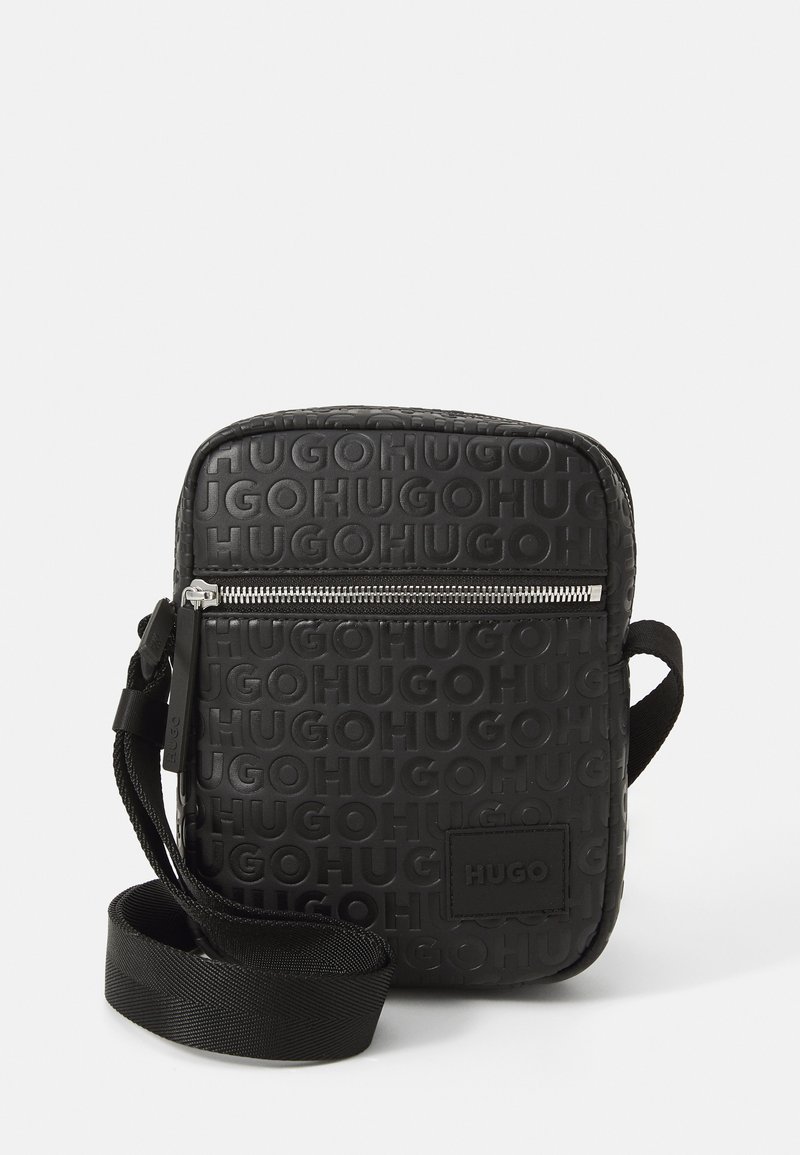 Černá obdélníková crossbody taška vyrobená z texturovaného materiálu, s embosovanou značkou, stříbrným zipem a tkaným popruhem.
