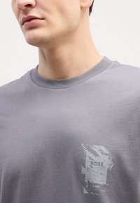 Grijze katoenen t-shirt met een ronde hals en een versleten logo grafiek op de linkerborst, met een gladde textuur.