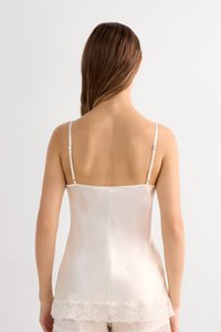 Satintopp i mjuk elfenben med justerbara axelband och spetskantdetalj vid fållen. Mjuk textur och figurnära design som framhäver ryggsilhuetten.
