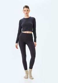 Tummanharmaa ribbed crop top ja siihen sopivat korkeavyötäröiset legginssit, yhdistettynä vaaleanbeigeihin neulottuihin sukkiin lisäämään tekstuuria.