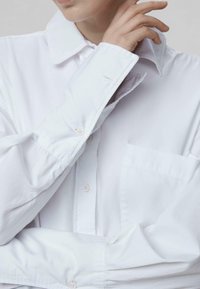 Witte overhemd met knopen, gemaakt van gladde stof, met een kraag, lange mouwen en een borstzak. Eenvoudig ontwerp zonder patronen.
